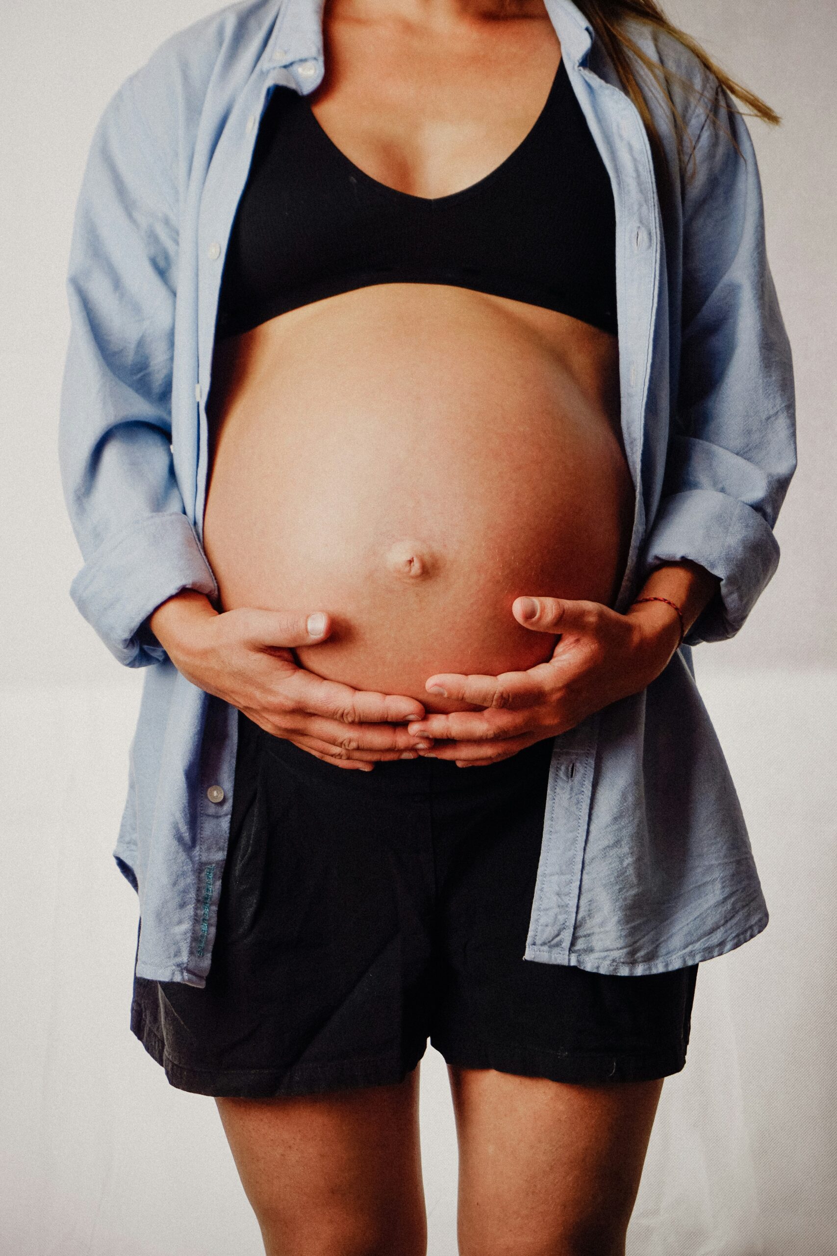 Femme enceinte debout, les mains posées sous le ventre en fin de grossesse